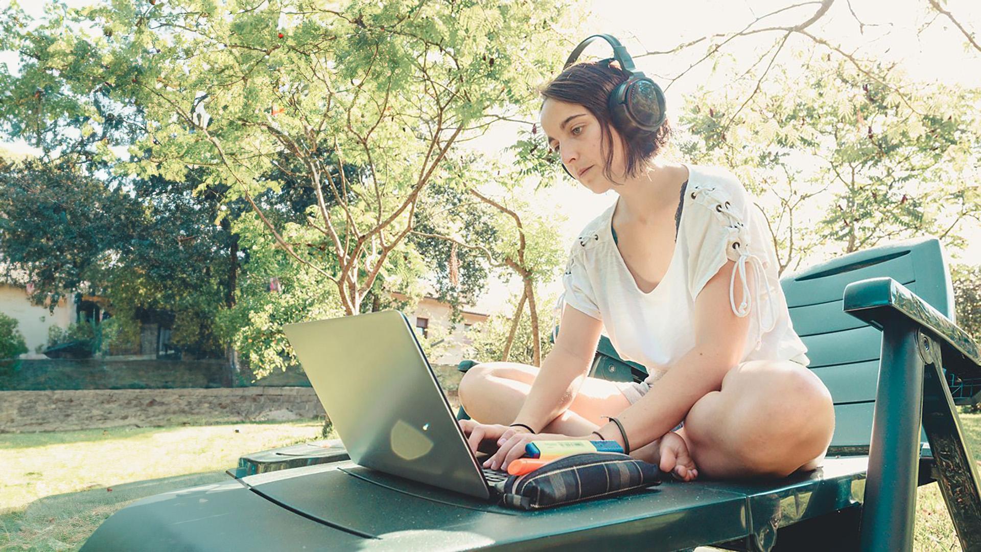 A young woman uses a laptop on an outdoor lounge chair.