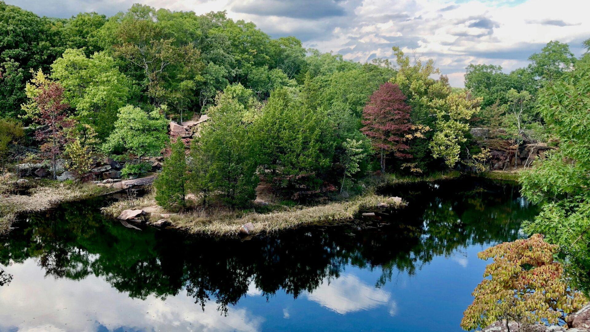 Rural landscape with a bright blue river, green trees and clouds reflecting over the water