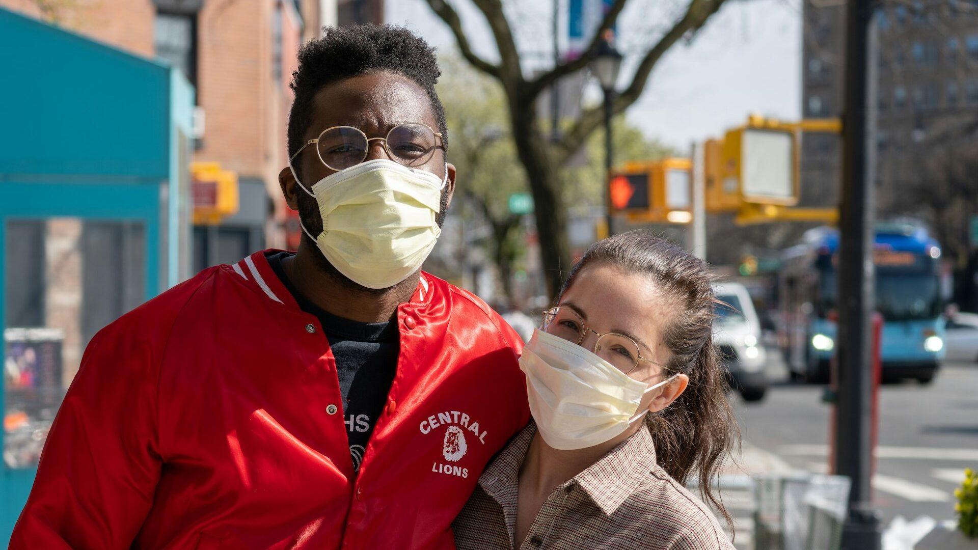 A man and woman in face masks on a sunny street