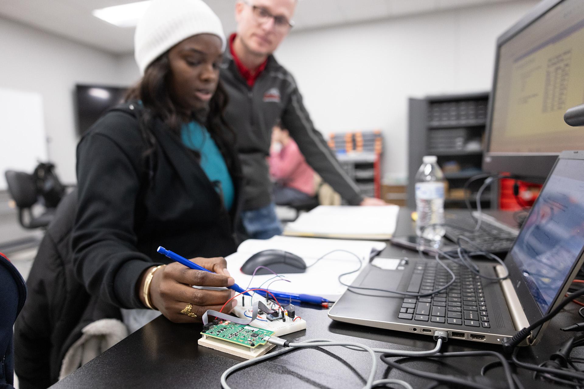 Black female student working on computer hardware with an instructor during a computer engineering class on a college campus.